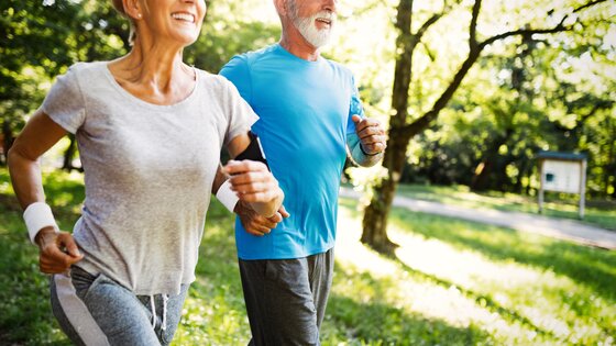 Ein älterer Mann und eine ältere Frau joggen in einem Park. | © AdobeStock-272938937