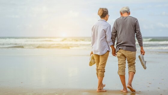 Ein Paar geht Hand in Hand an einem Strand entlang. | © AdobeStock-294409957