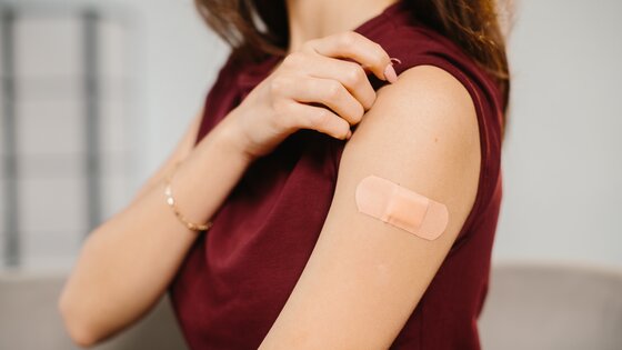 Eine Frau mit einem Pflaster auf dem Oberarm | © AdobeStock_1860427692