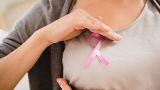 Eine Frau hält eine rosa Schleife, das Symbol für Brustkrebs, auf ihrer Brust. | © AdobeStock_473151953