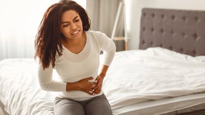 Eine Frau mit schmerzverzerrtem Gesicht auf einem Bett. | © AdobeStock_1089846744
