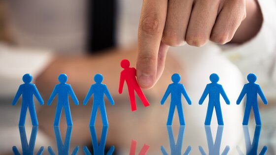 Eine rote Scherenschnittfigur wird aus einer Reihe von blauen herausgenommen (Symbolbild). | © AdobeStock_209445070