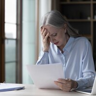 Eine Frau sitzt am Tisch und stützt verzweifelt den Kopf in die rechte Hand. | © AdobeStock-503248405