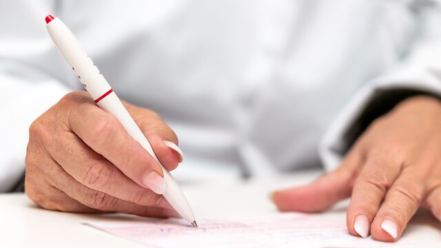 Eine Hand hält einen Stift, damit wird ein Rezept unterschrieben.  | © AdobeStock 249986710