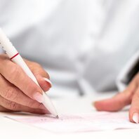 Eine Hand hält einen Stift, damit wird ein Rezept unterschrieben.  | © AdobeStock 249986710