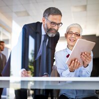 Ein Mann und eine Frau betrachten in einem Büroraum einen Tabletbildschirm. | © AdobeStock-305938477