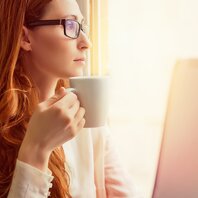 Eine rothaarige Frau schaut aus dem Fenster, sie hält eine Tasse in der Hand. | © AdobeStock-134084317